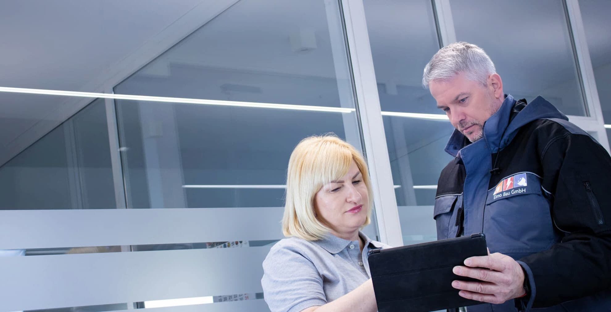 Starten Sie Ihr Projekt bei uns! Die Geschäftsführerin zeigt mit der Hand auf ein Tablet. Neben ihr steht ein Mitarbeiter und hält ein Tablet in der Hand.